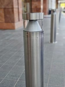 A modern stainless-steel outdoor lamp standing on a tiled walkway in BKC, Mumbai. It is a clean, minimal design that looks sleek and stylish. 