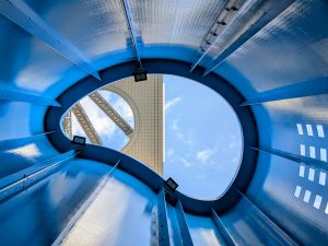 A view from inside a rounded, blue structure, looking up at a bright sky with clouds. 