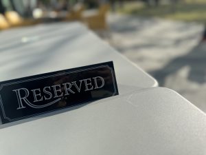 A close-up of a black and white “Reserved” sign placed on a light gray outdoor table.