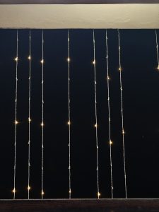 A dark background features multiple strands of warm white fairy lights hanging vertically. 