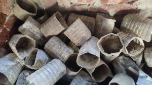 A close-up image of a pile of used, clear or translucent plastic bottles that have been cut in half or had their tops removed, likely for recycling or gardening use. They are stacked against a red brick wall.