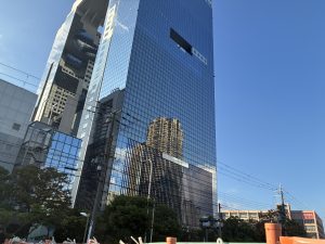 A tall, modern glass skyscraper reflects the blue sky and surrounding buildings.