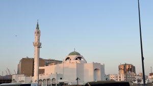 A beautiful white mosque with a tall minaret and a green dome stands out against a clear blue sky.