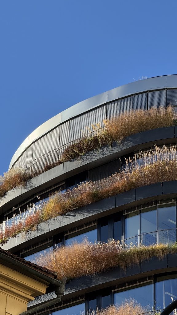A modern building with a curved roof is adorned with lush greenery along its terraces