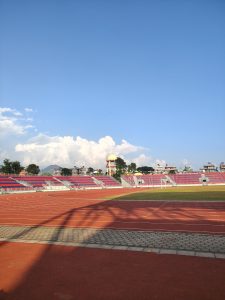 A view of a sports stadium featuring red and blue bleachers under a clear blue sky with a few white clouds.
