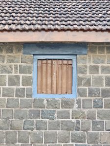 A closed wooden window with a blue frame on a stone building wall with a tiled roof near Elephanta caves in Mumbai, Maharashtra. 