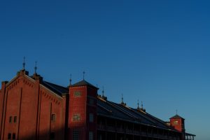 Old red brick architecture under a clear blue sky in golden hour light. The spires and shadows give it a nostalgic, dramatic feel.