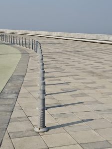 A row of short grey bollards curves along a tiled walkway near the sea. The clean, open space creates a modern look. Photographed in Mumbai, Maharashtra.