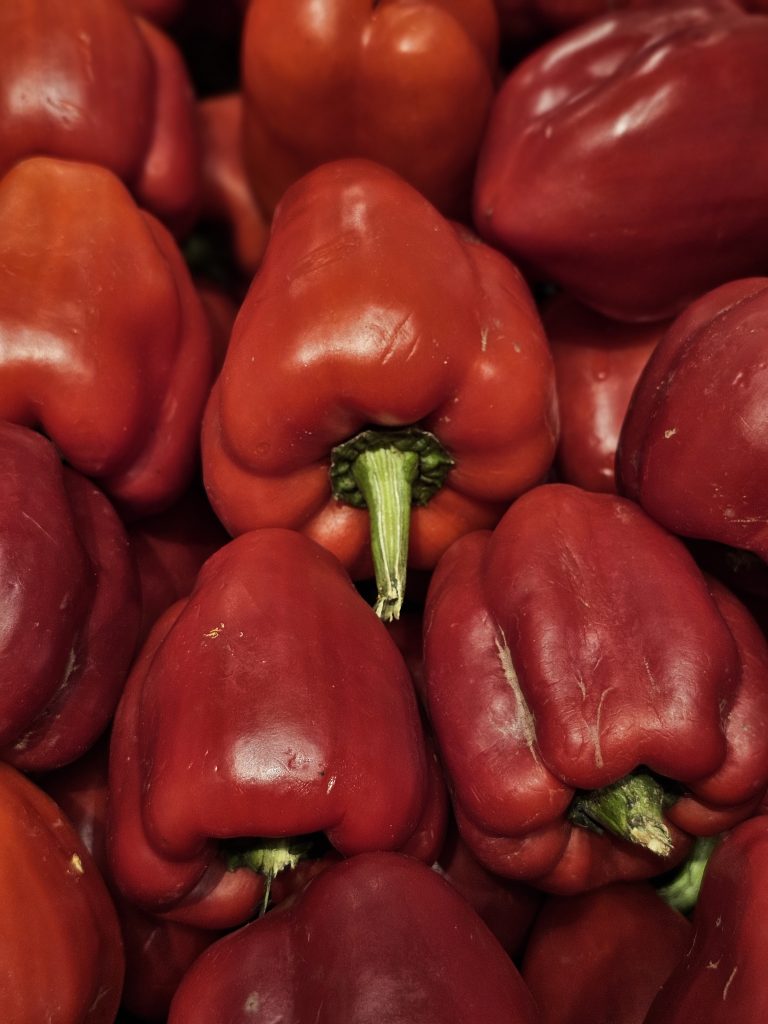 Bright red capsicums with smooth, glossy skin are arranged closely at a hypermarket in Kozhikode, Kerala. The rich color and fresh stems give the vegetables a bold, striking look.