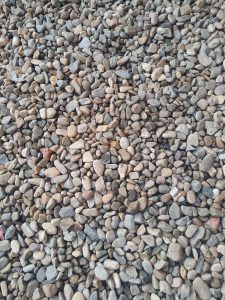 A close-up view of a varied assortment of small, smooth pebbles and stones, predominantly in shades of brown, gray, and beige. 