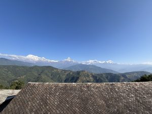 A panoramic view of snow-capped mountains against a clear blue sky, with green hills in the foreground.