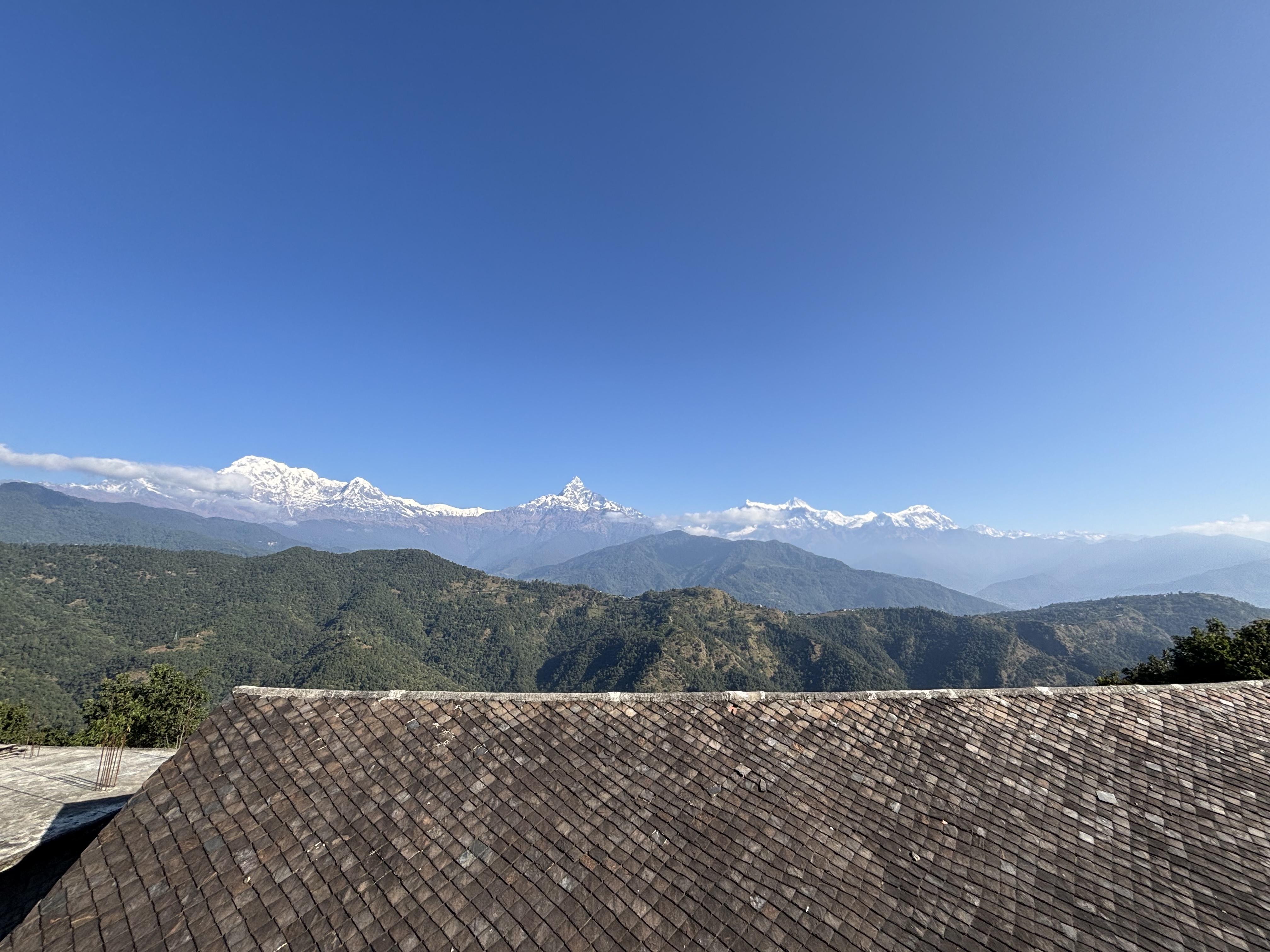 A panoramic view of snow-capped mountains against a clear blue sky, with green hills in the foreground.