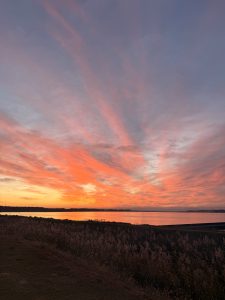 A sunset sky filled with clouds, with the area near the lake&rsquo;s horizon glowing golden.