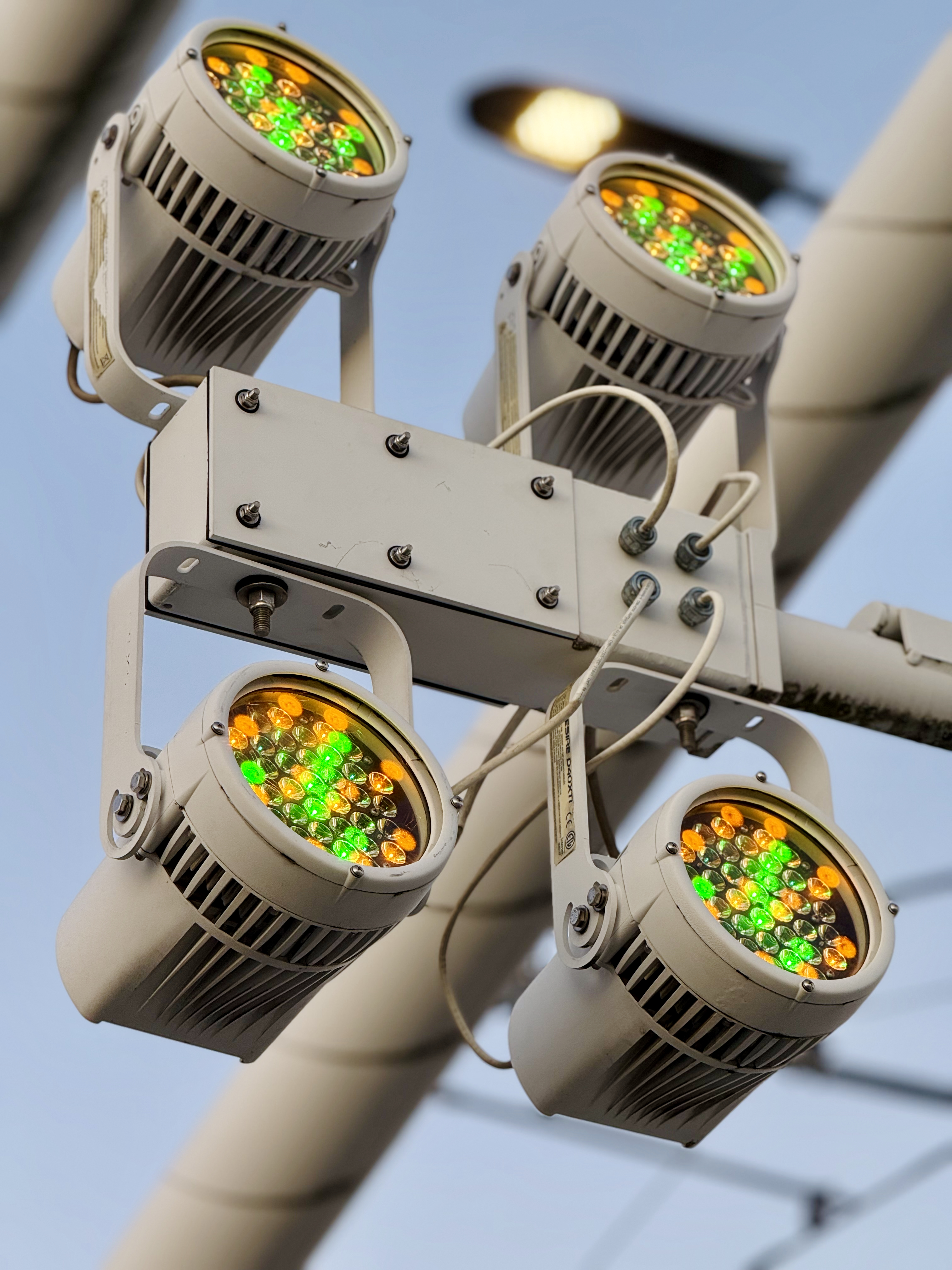 A close-up view of bright LED lights on the Tilikum Crossing Bridge in Portland. The lights glow in green and amber colors, fixed to a metal frame against the clear evening sky.