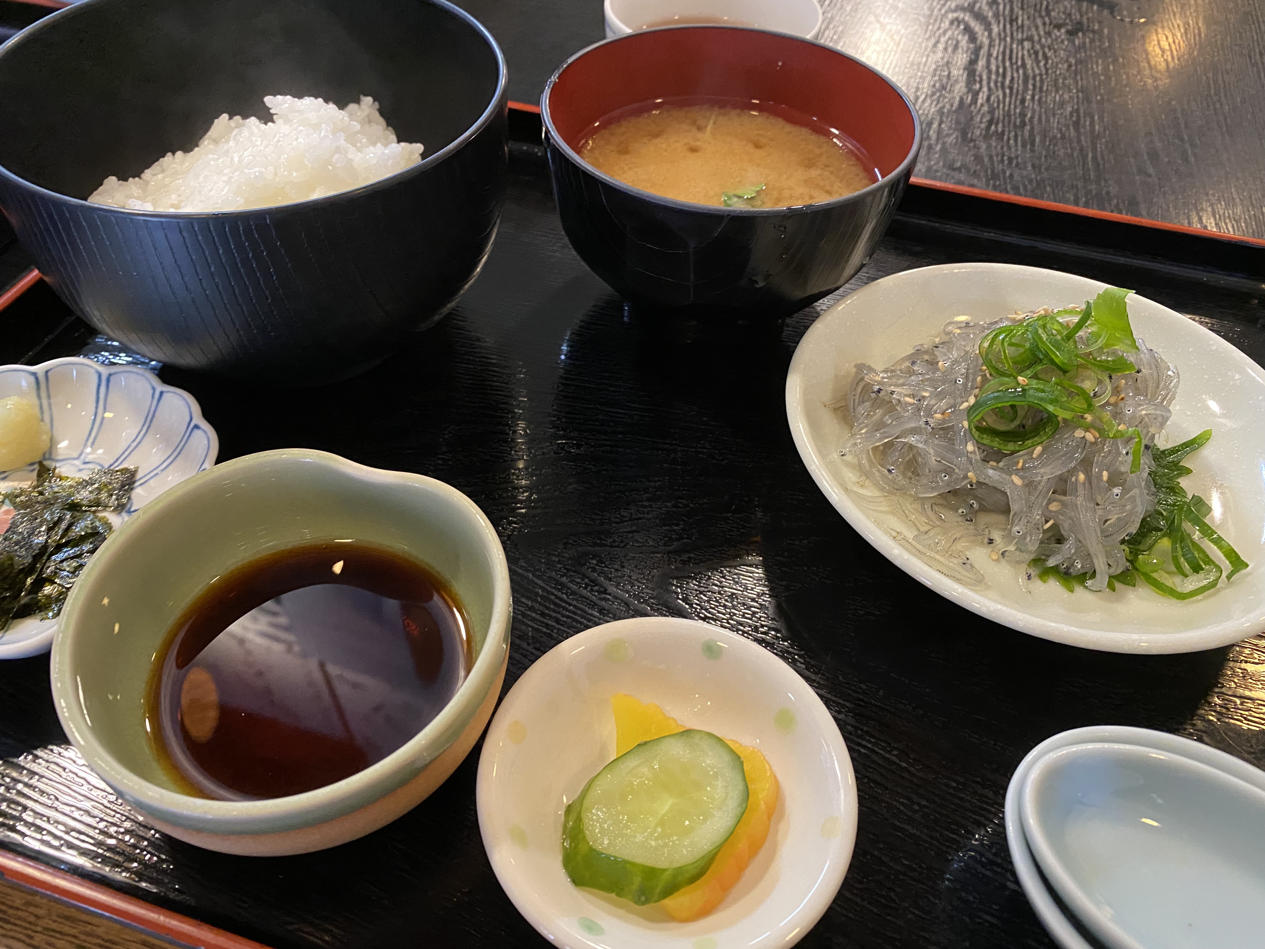 A black bowl of steaming white rice sits next to a red bowl of miso soup with a sprinkle of green herbs.