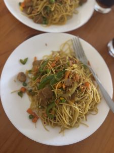 chowmein with garnish and sausage on a white plate
