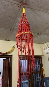 A handcrafted decorative lantern made of red and yellow threads, featuring beads and colorful embellishments, hanging from the ceiling