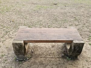 An old wooden bench with stone legs stands on dry ground near the Elephanta Caves, Mumbai, offering a simple resting place for visitors. 