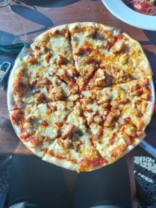 A circular pizza topped with melted cheese, pieces of chicken, and a red tomato sauce on a golden crust, sitting on a wooden table.
