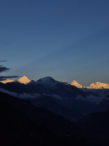 A panoramic view of snow-covered mountains under a twilight sky, with the peaks illuminated by the last rays of sunlight.