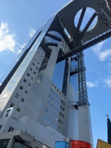 A tall, modern building in Osaka, Japan, featuring a striking architectural design with a large circular opening at the top.