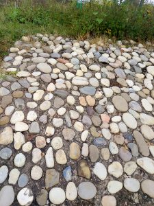 A close-up view of a pathway or area covered with a variety of smooth, rounded stones in different shades of gray, beige, and cream.