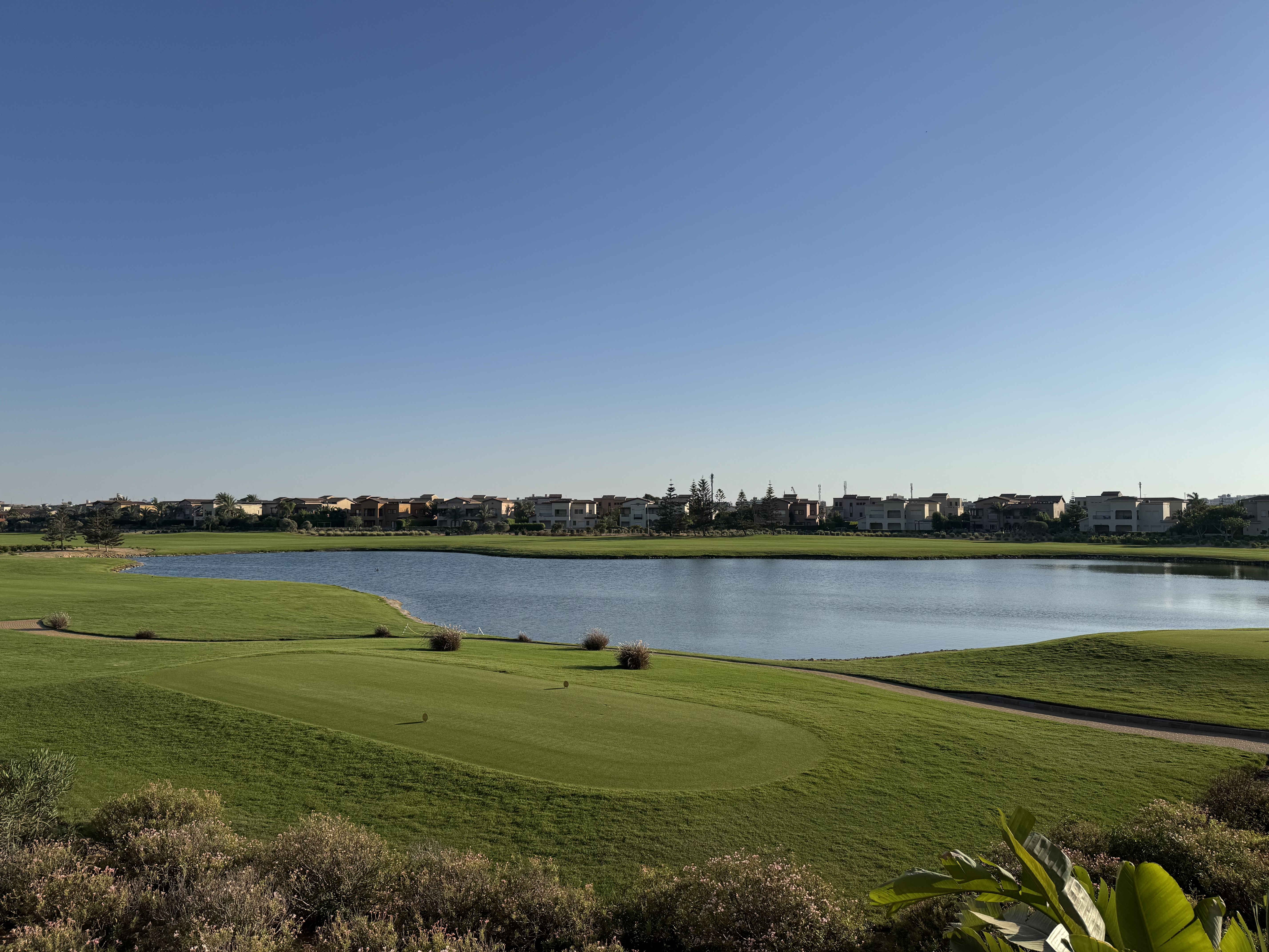 Golf field view in Marassi with houses on the other side and a pond in between the green field, Egypt.
