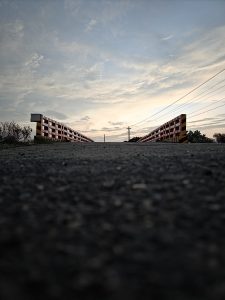 A close-up shot of an asphalt road, taken from ground level and looking straight through a small bridge. The photo was taken at sunset, with white clouds in the sky reflecting the sunlight.