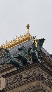 A close-up view of a decorative architectural feature on a building, showcasing ornate sculptures of horses and a winged creature on a pediment.
