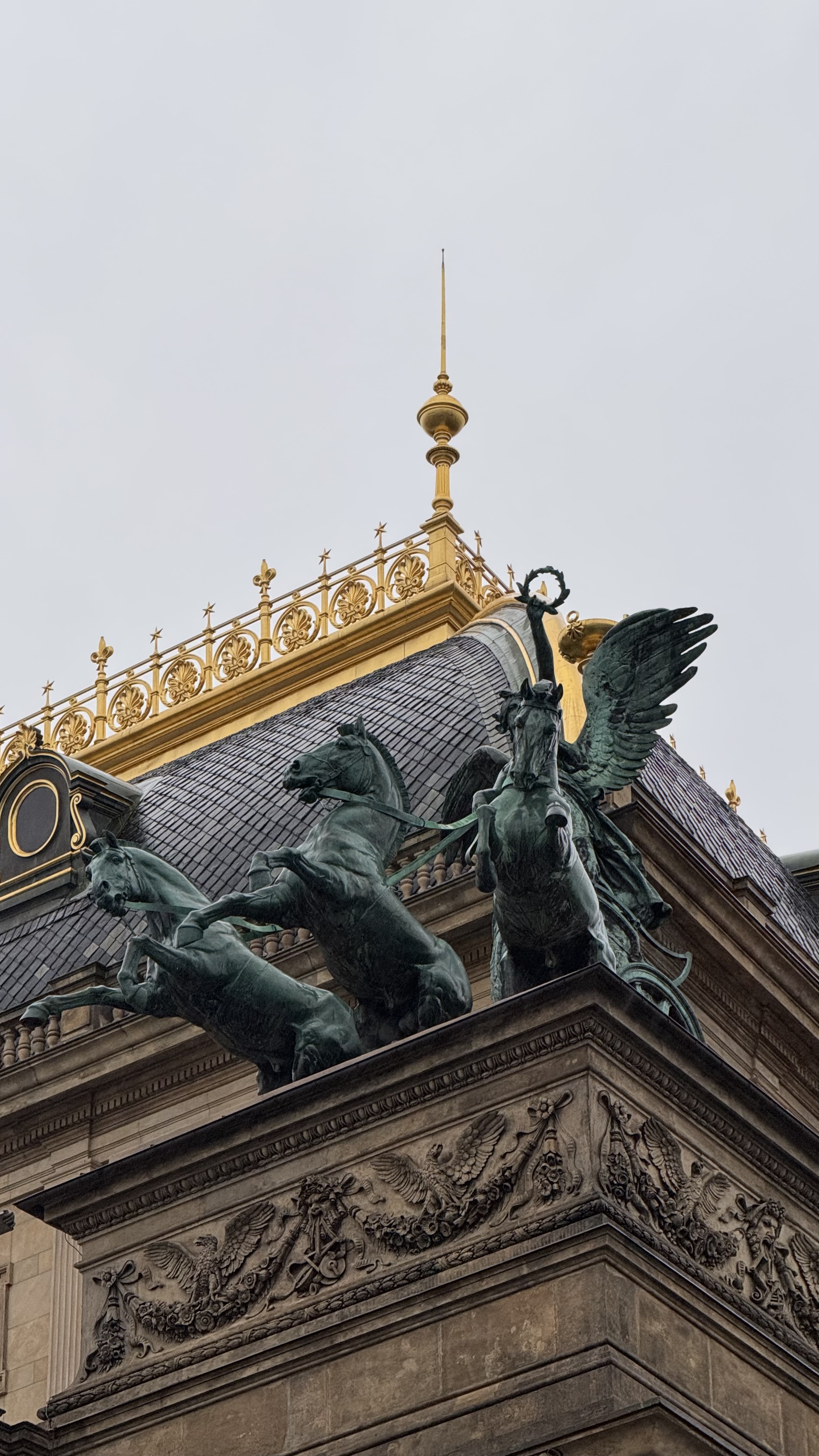 A close-up view of a decorative architectural feature on a building, showcasing ornate sculptures of horses and a winged creature on a pediment. 