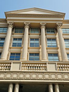 A modern cream-colored building with tall Corinthian-style pillars and large windows under a triangular roof. Location: Mumbai, Maharashtra. 
