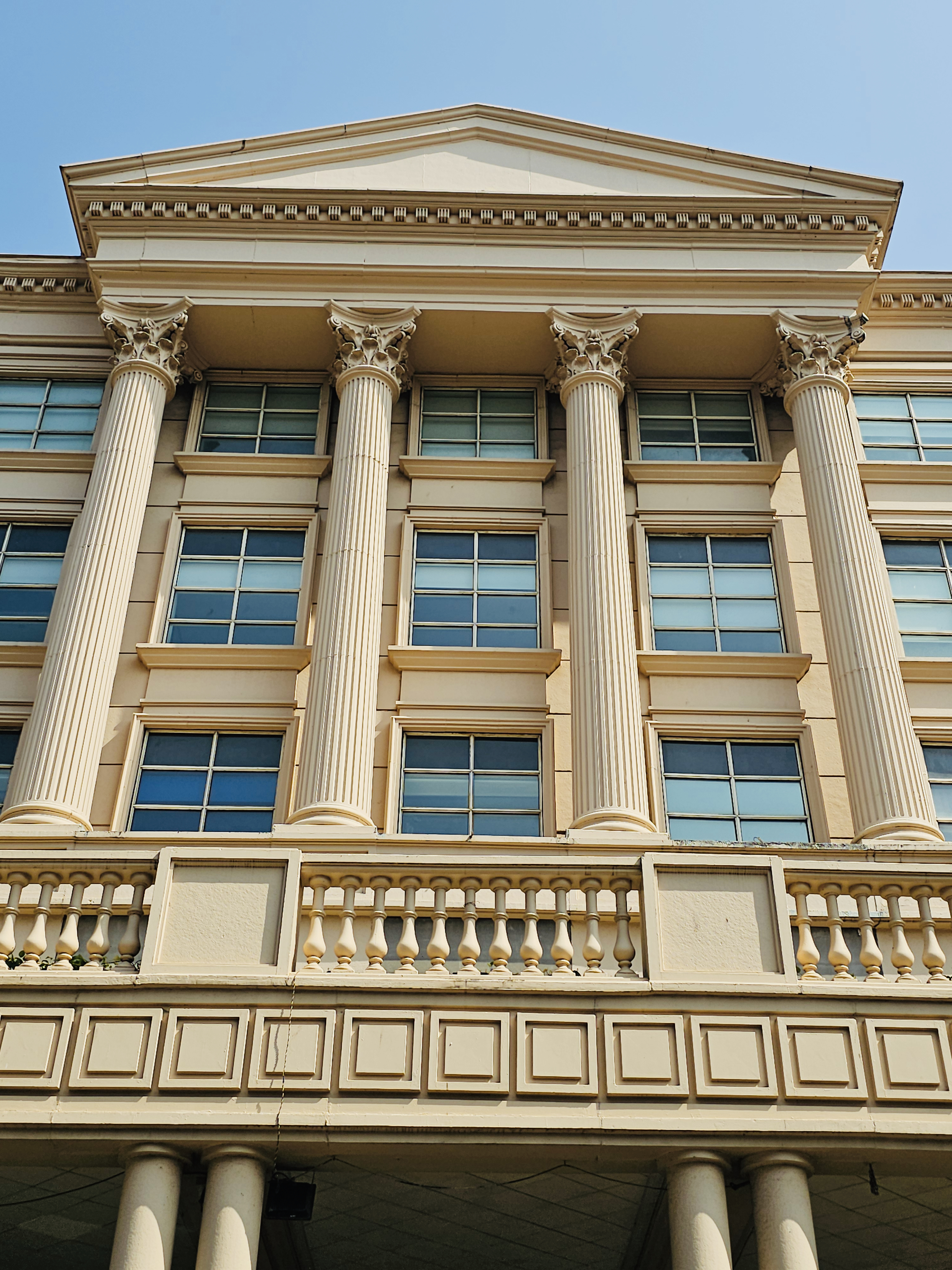 A modern cream-colored building with tall Corinthian-style pillars and large windows under a triangular roof. Location: Mumbai, Maharashtra. 