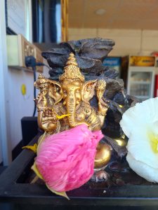 A golden statue of the Hindu deity Ganesha, depicted with an elephant head and multiple arms, is situated among dark, textured rocks. 