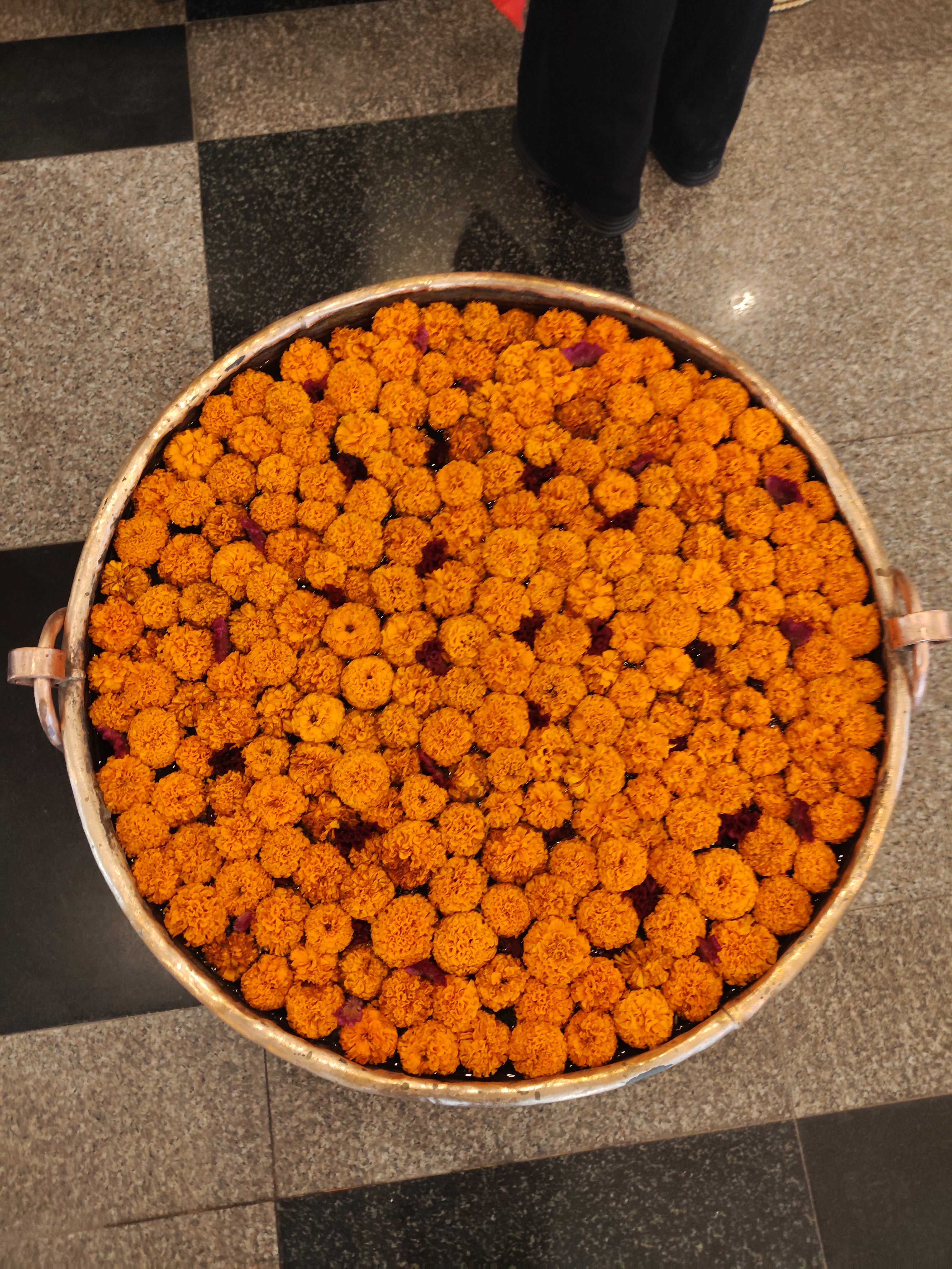 A circular metal tray is filled with vibrant orange marigold flowers, creating a dense, colorful display. 