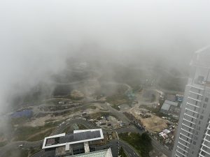 A foggy, high-altitude view of Genting Highlands, Malaysia, with clouds drifting around the buildings and winding mountain roads, revealing bits of the landscape and construction areas.