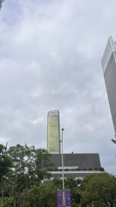 A tall, modern skyscraper stands prominently against a backdrop ofovercast skies.