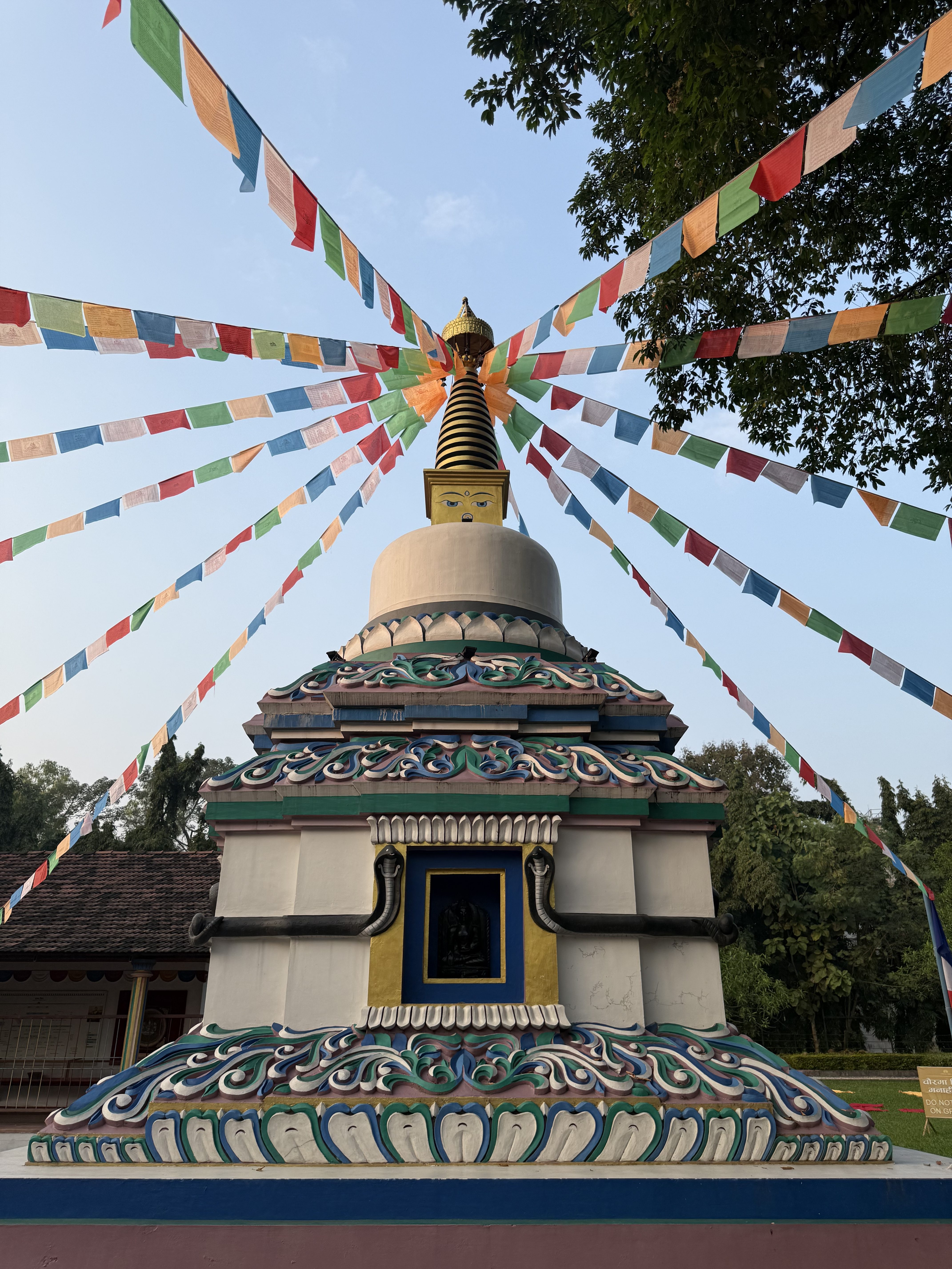 The picture shows a Buddhist stupa with a golden conical striped design at the top. Below, it is painted with the Buddha's eyes, and from the top, strings of colorful prayer flags hang down.