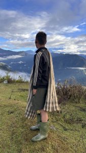 A person stands on a grassy hilltop overlooking a mountainous landscape