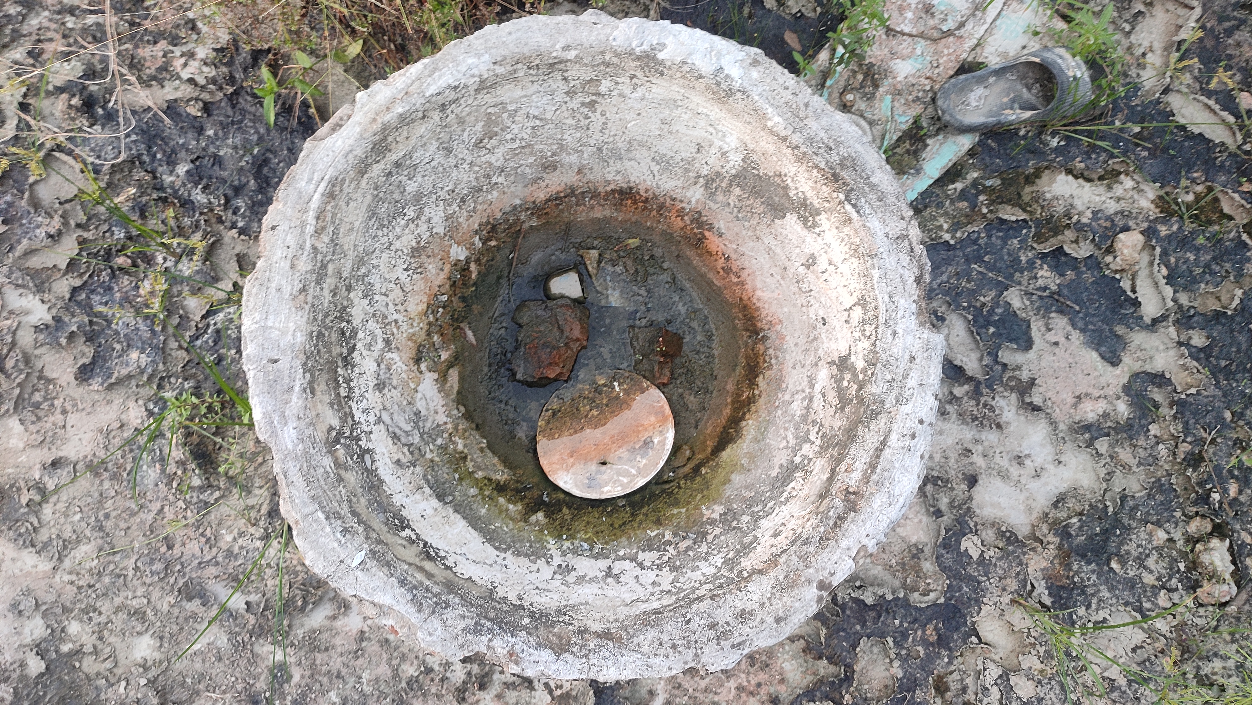 A round cement pit filled with dirty water and a circular object, seen from above on patchy ground.