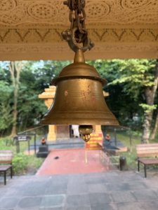 A picture focused on a bell hung on the ceiling. The background seems like a Hindu temple with trees surrounding it.
