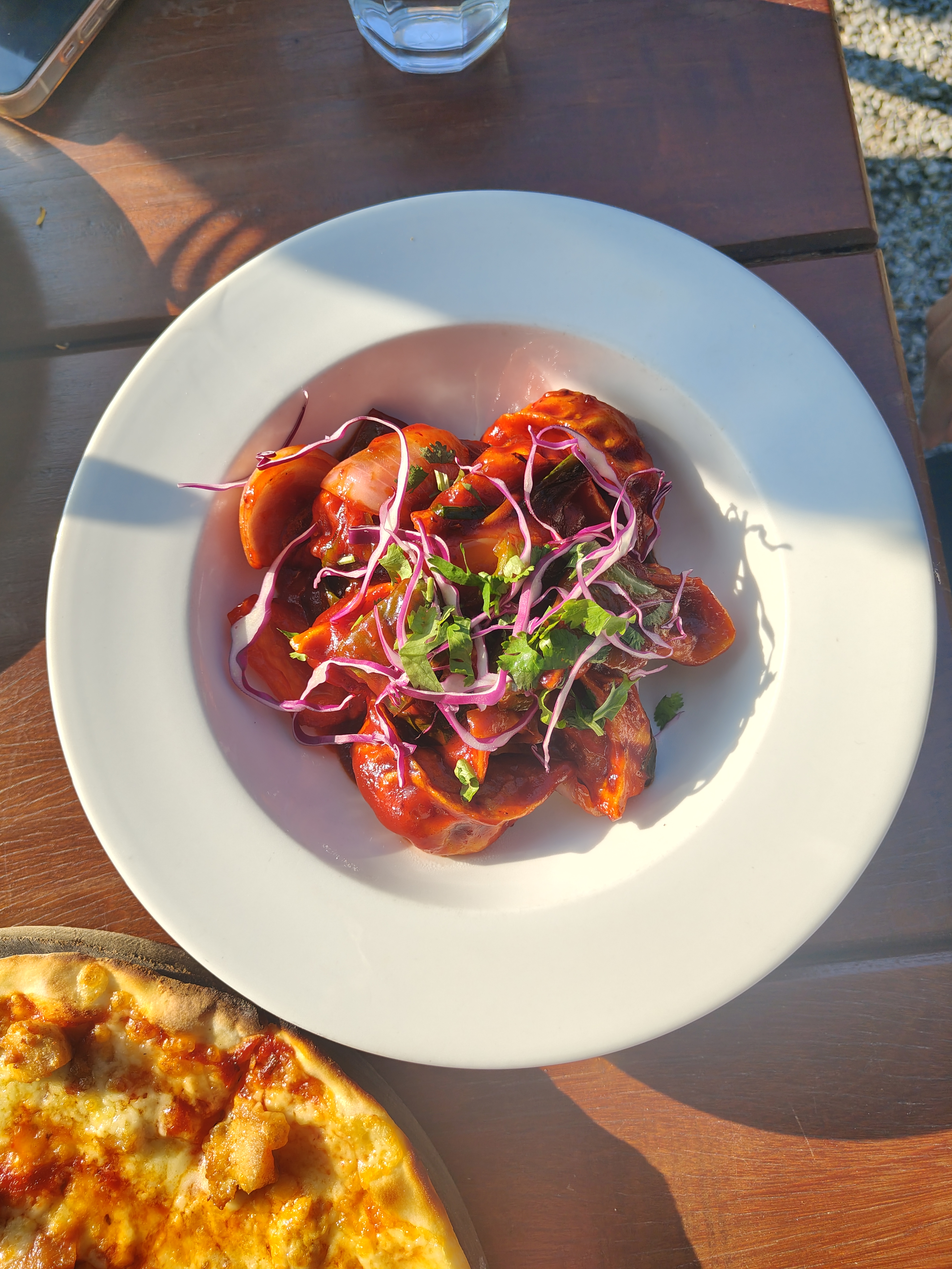 A white plate filled with colorful momos, beautifully glazed and topped with fresh herbs and thin slices of red cabbage.