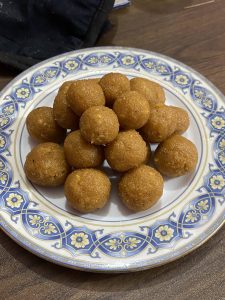 A plate of golden-brown sweet naru treats is neatly arranged on a decorative blue and white dish, resting on a wooden table. The mood is inviting and warm.