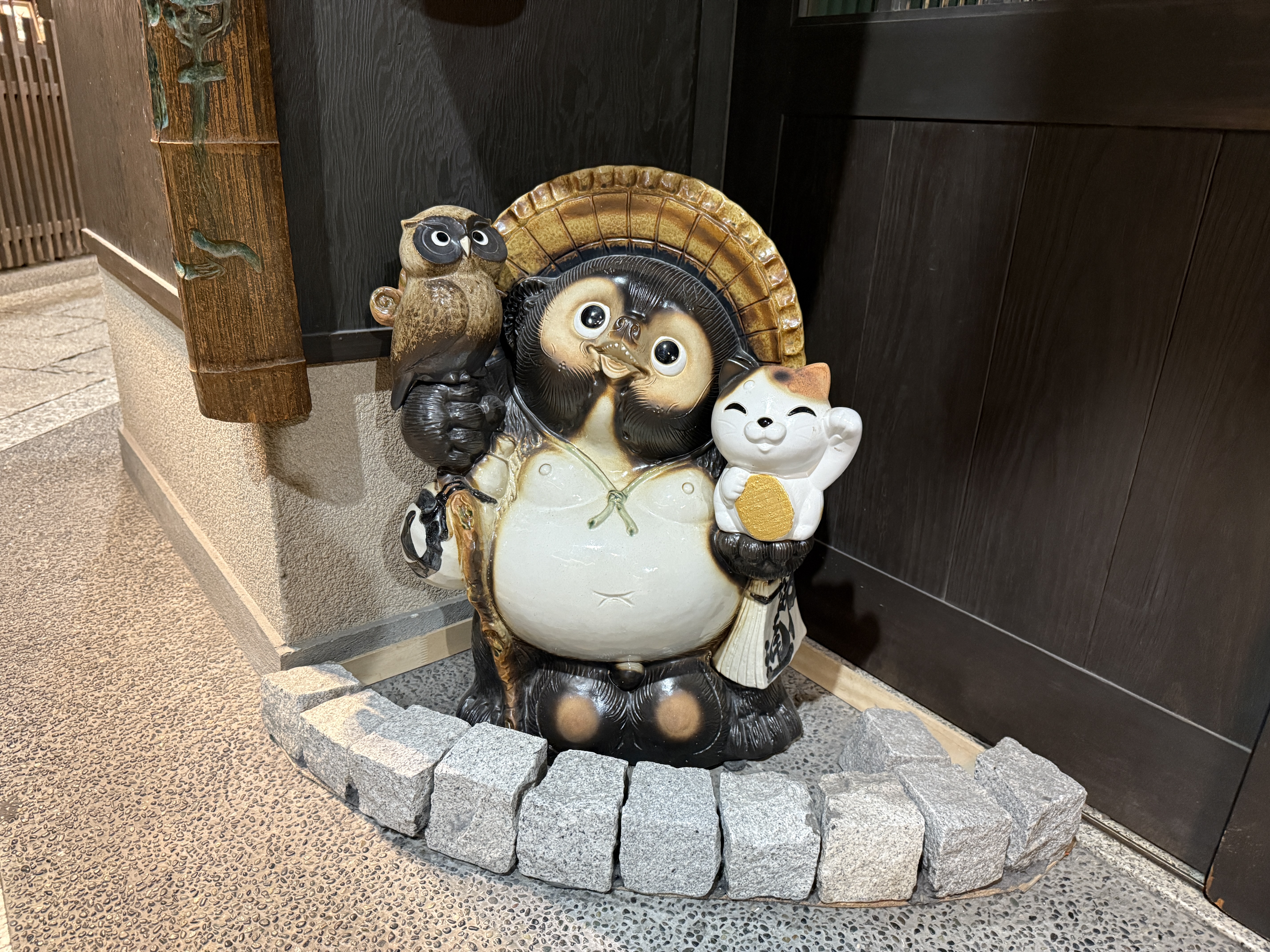 A Shigaraki tanuki statue with a straw hat and smile stands outside a Japanese home, bringing luck and warmth.