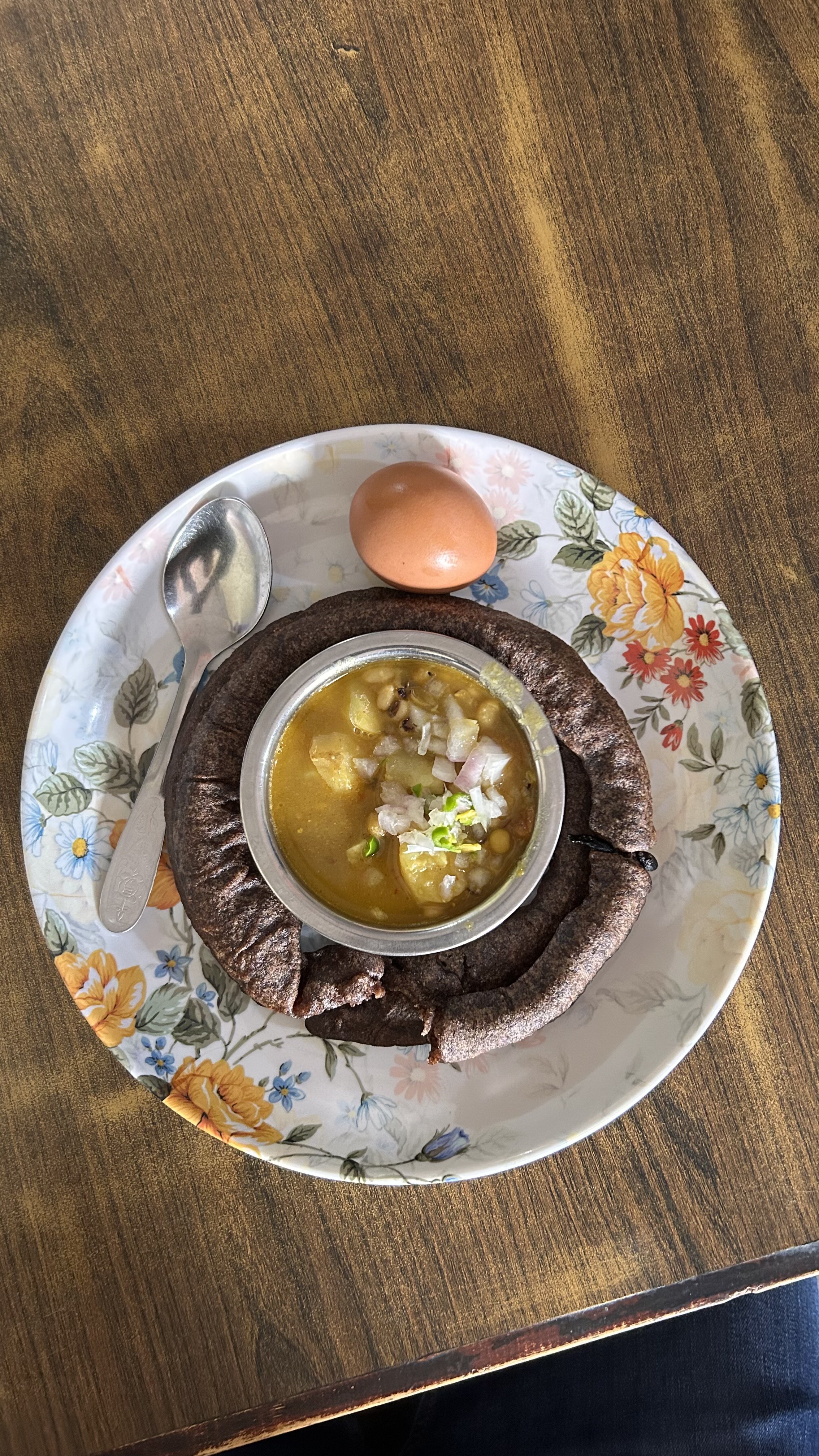 A floral plate with yellow lentil curry topped with onions and chilies, served inside a dark, bowl-shaped whole-grain bread.