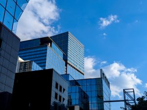 A view of modern skyscrapers with reflective glass façades against a bright blue sky filled with scattered clouds.