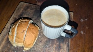 
A cup of milk and buttered bread on a wooden board in dim early-morning light.