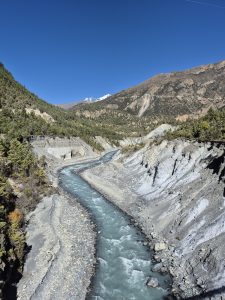 A winding river flows through a rocky valley surrounded by steep, rugged mountains and dense patches of greenery.