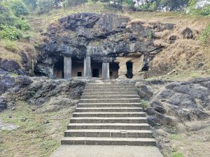 A view of a simple rock-cut cave temple with stone pillars and stairs leading up to it. Captured at Elephanta Caves, Mumbai, Maharashtra. 