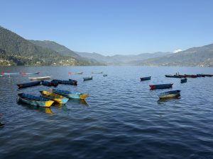 A serene lake scene featuring several small boats in various colors, including blue and yellow, floating on the calm water.