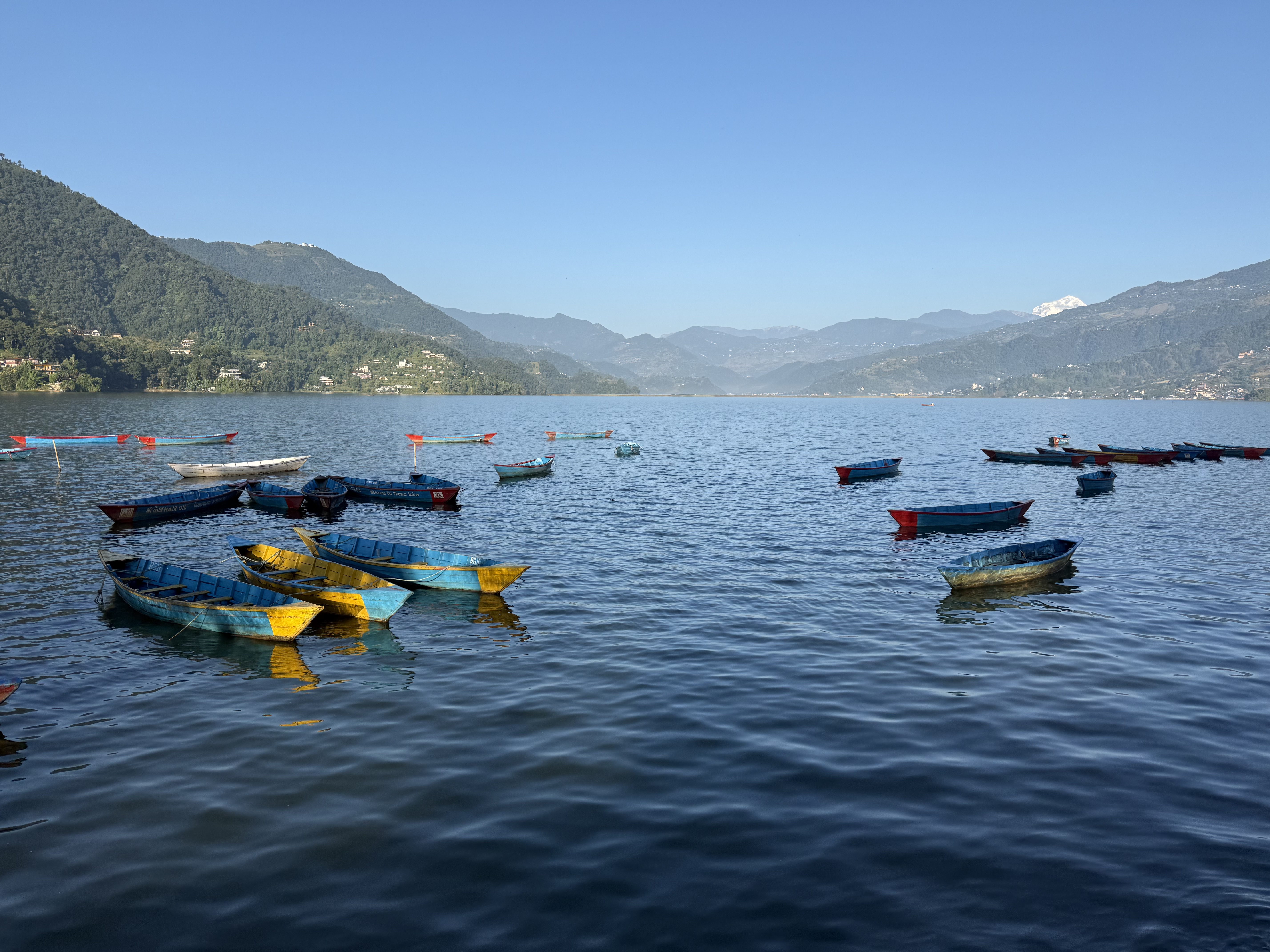 A serene lake scene featuring several small boats in various colors, including blue and yellow, floating on the calm water.